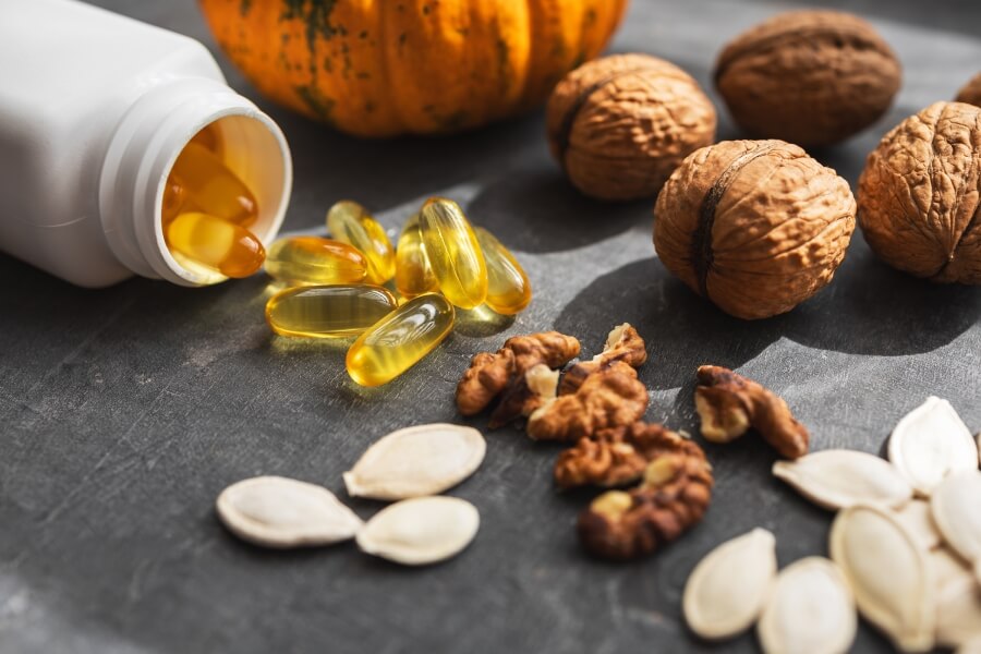 : Kapsle s omega-3 mastnými kyselinami vysypané z lahvičky mezi vlašskými ořechy a semínky – doplněk stravy a potravinové zdroje omega 3