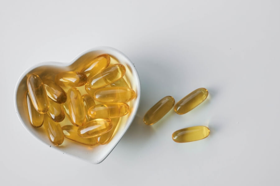 Žluté kapsle omega-3 rybího oleje v misce ve tvaru srdce na bílém pozadí – podpora zdraví srdce a cév