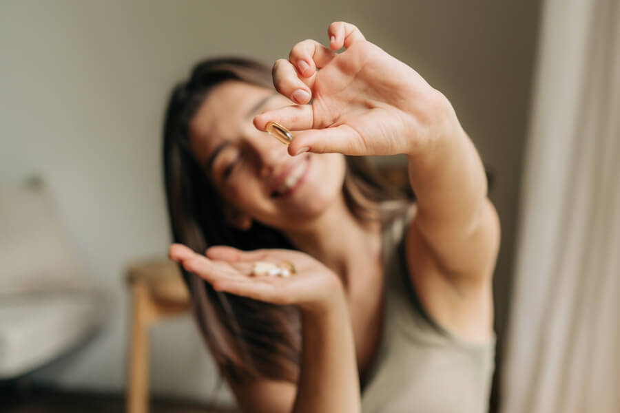 Mladá žena drží kapsli omega-3 doplňku stravy a usmívá se, ilustrační foto užívání omega-3 mastných kyselin pro podporu zdraví