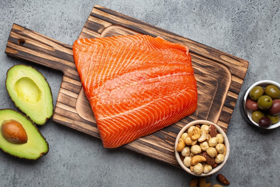 Čerstvý losos, avokádo, ořechy a olivy na prkénku – potraviny bohaté na omega 3 mastné kyseliny a zdravé tuky