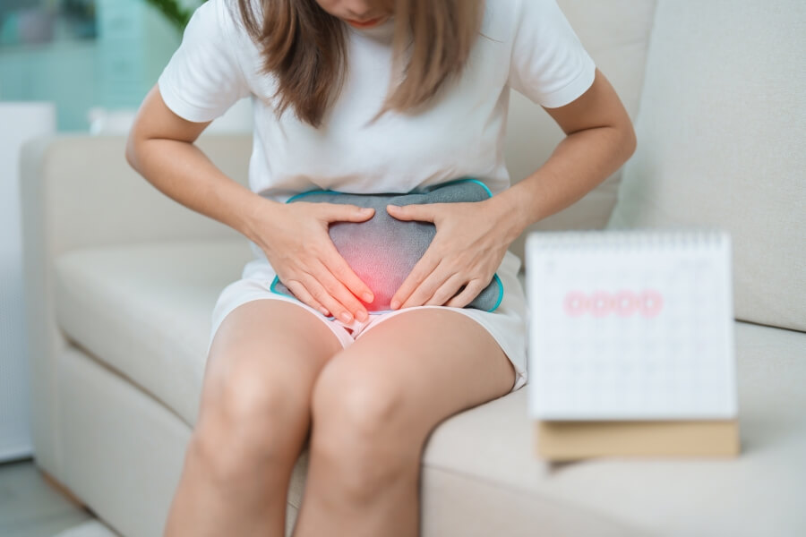 Žena s menstruační bolestí přikládá termofor na podbřišek; ilustrační foto, jak mohou omega-3 mastné kyseliny pomáhat zmírnit menstruační křeče a zánět