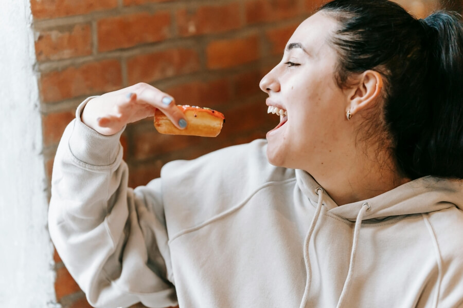 Žena s chutí kouše do sladkého pečiva jako ilustrace zvýšené chuti na jídlo a hedonického jedení po dietě, které přispívají k jojo efektu.